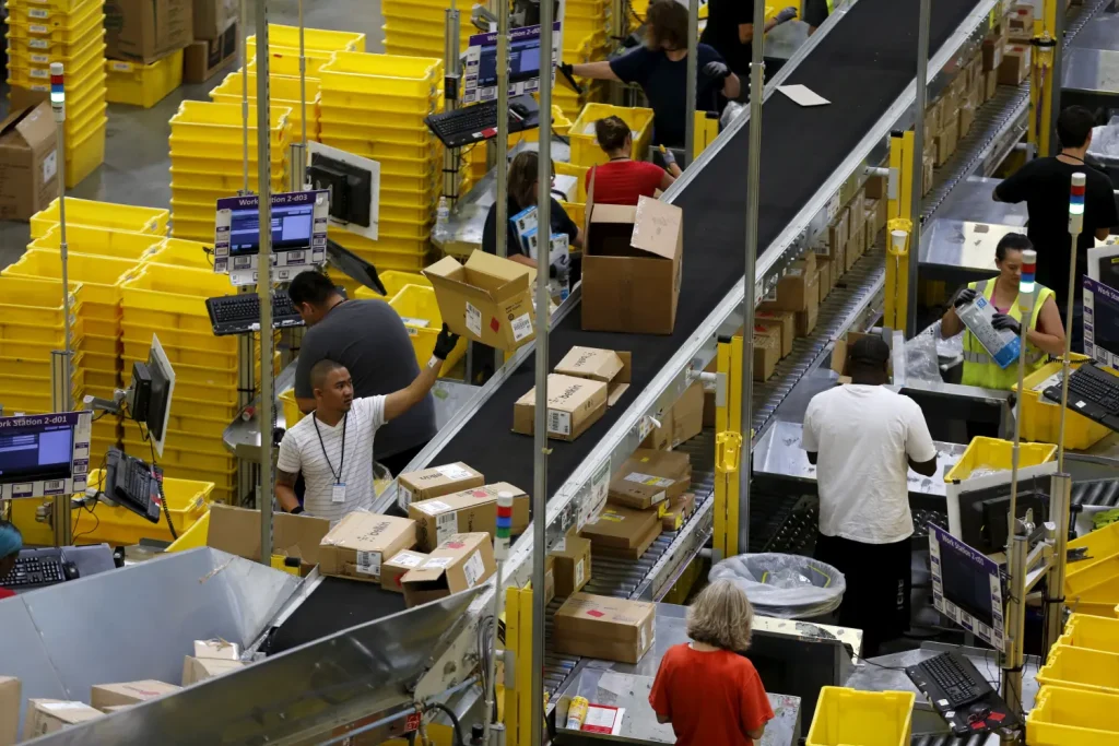 Warehouse workers sorting packages on a conveyor belt in a busy distribution center, representing the impact of e-commerce on logistics.